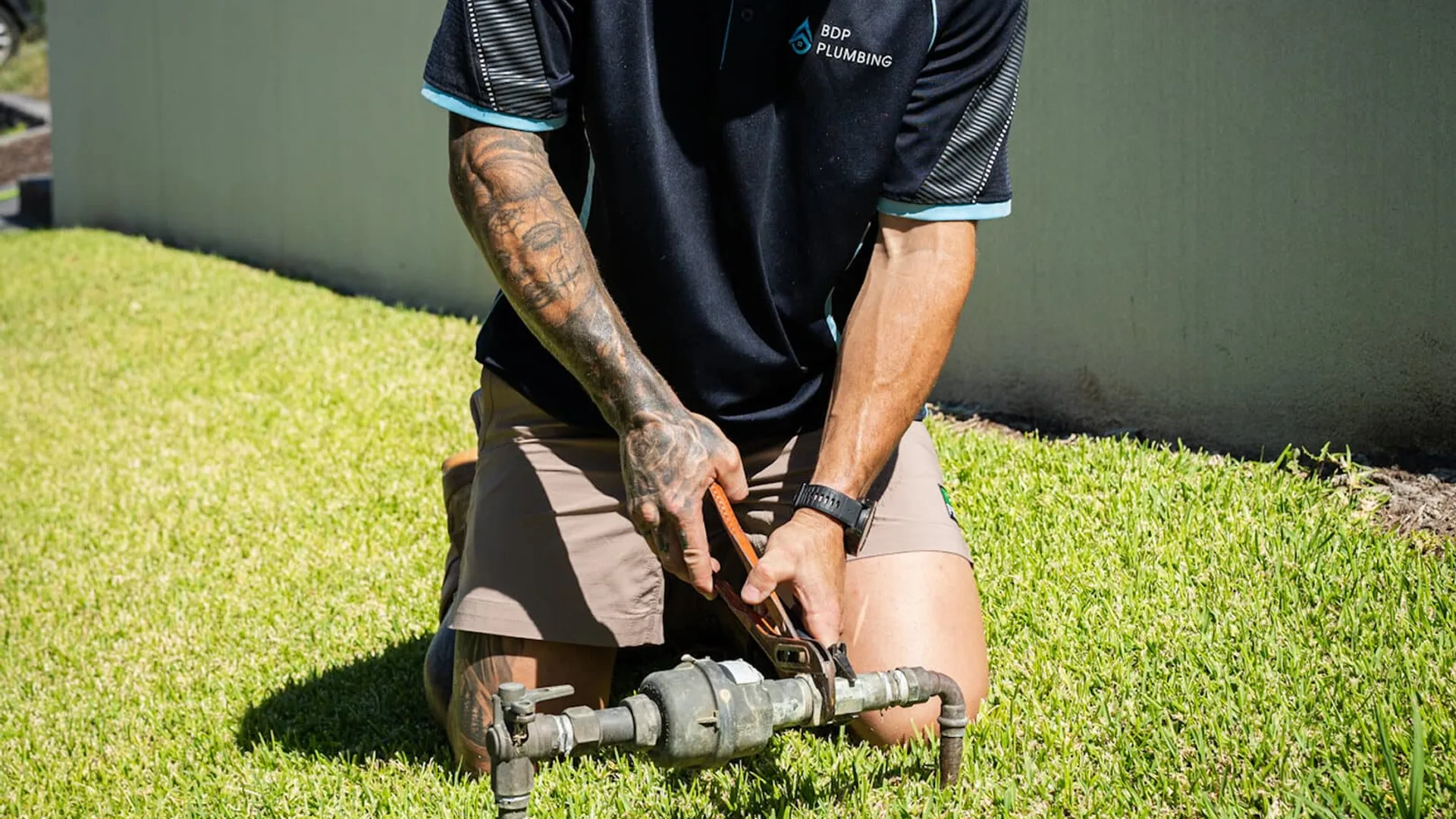 Plumber kneeling at a water meter on a front lawn